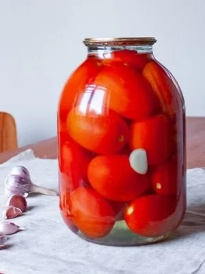 A jar of vibrant pickled tomatoes with herbs and spices